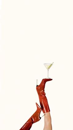 a woman holding a martini glass up in the air with her legs stretched out to catch it