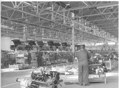 an old black and white photo of men working in a factory with cars on the assembly line