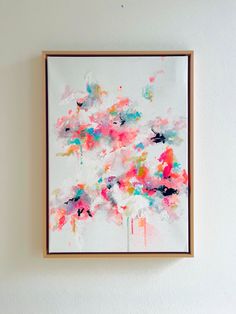 an abstract painting hangs on the wall in front of a white wall with a wooden frame