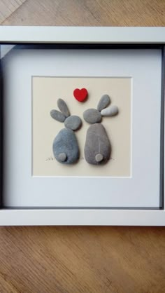 two rocks in the shape of rabbits with a red heart on their backs are placed inside a white frame