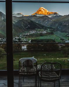 two chairs sitting on top of a wooden deck next to a table with a view of mountains in the distance