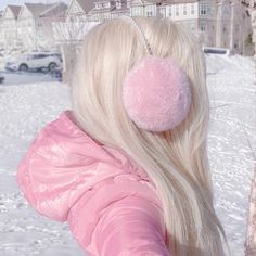 a woman with long blonde hair wearing a pink jacket and ear muffs in the snow