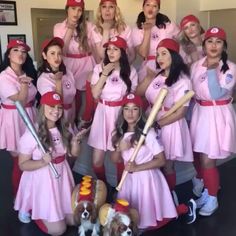 a group of women in pink dresses holding baseball bats and posing for a photo with a dog