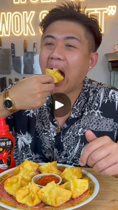 a man eating food from a plate on top of a wooden table in front of a neon sign