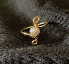 a gold ring with a white bead on the middle and a twisted wire around it