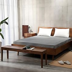 a bed with white pillows and gray sheets in a room next to a plant on the floor