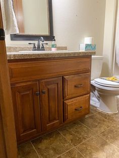 a white toilet sitting next to a wooden sink vanity in a bathroom under a mirror