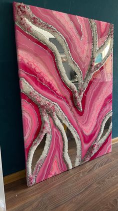 a pink and silver painting sitting on top of a wooden floor next to a blue wall