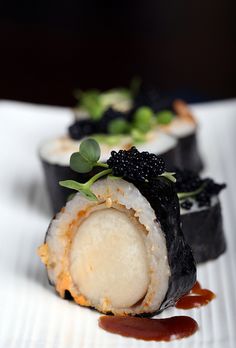 two sushi rolls on a white plate with sauce and black cauliflower garnish