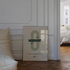 a poster on the floor next to a bed in a room with white walls and wood floors