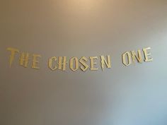 the word the chosen one is cut out of gold foil on a white wall in a room