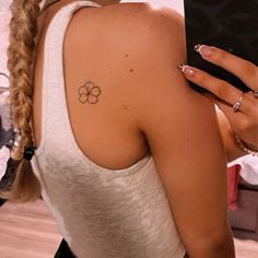 a woman with a flower tattoo on her back shoulder holding a cell phone in her right hand