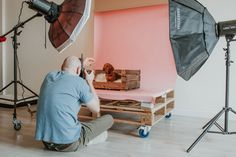 a man sitting in front of a camera on top of a wooden pallet next to a pink wall