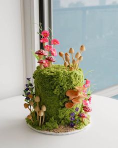 a green cake with mushrooms and flowers on it sitting on a table next to a window