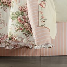 a bed with pink and white floral comforters on it's sides, next to a striped pillow case