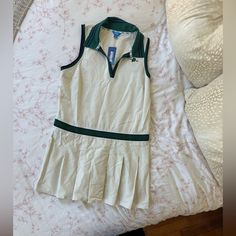 a white and green tennis dress laying on top of a bed next to an unmade pillow