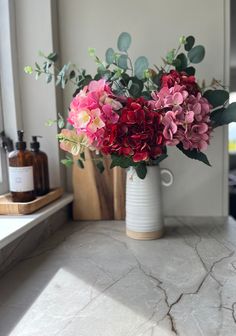 a vase filled with pink and red flowers sitting on top of a counter next to a window