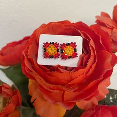 a pair of flower shaped earrings sitting on top of a bouquet of red and yellow flowers