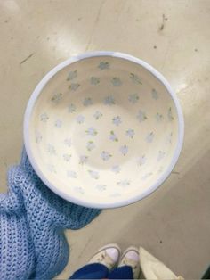 a person holding up a white bowl with blue flowers on it and their feet in the air