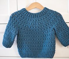 a blue crocheted sweater hanging on a wooden hanger