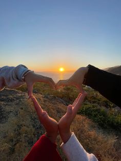 two hands making a heart shape with the sun setting in the back ground behind them