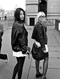 three women are standing on the sidewalk in front of a bridge and one is holding a cell phone