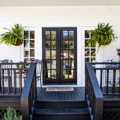 a porch with black railings and potted plants on the steps to a white house