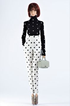 a woman in black and white polka dot print pants holding a handbag while standing next to a mannequin