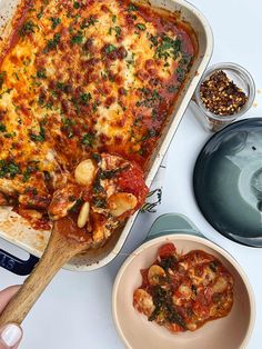 a person holding a wooden spoon in front of a casserole dish with meat and vegetables