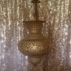 a gold colored lamp hanging from a ceiling in front of a curtained wall with sequins on it