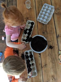 two children sitting at a table with trays of dirt and ice cubes in them