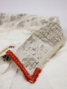 an old white scarf with red trim on top of a bed sheet and some sheets