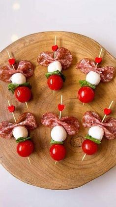 small appetizers with meat, tomatoes and cheese are arranged on a wooden plate