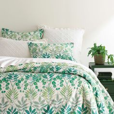 a bed with green leaves on it next to a nightstand and potted plant in the corner