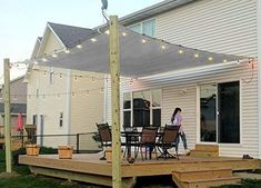 a woman walking across a deck next to a house with string lights strung over it