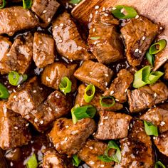 meat with sesame seeds and green onions on a wooden spoon next to some chopsticks