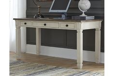 a desk with a computer on top of it in front of a painting and rug