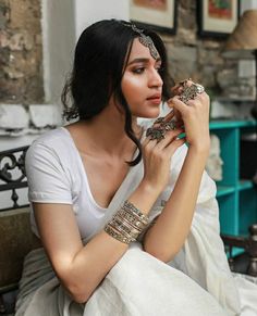 a woman sitting on top of a bed wearing bracelets and holding something in her hand