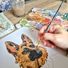 a person is painting a dog on paper with a brush and watercolor pencils