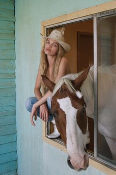 a woman is leaning on the window sill to pet a brown and white horse