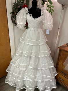 a white wedding dress on display in front of a door with balloons and greenery