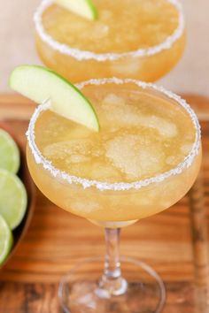 two margaritas sitting on top of a wooden cutting board