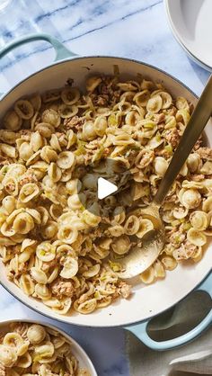 a pot filled with pasta and meat on top of a table next to two bowls