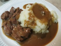 a white plate topped with meat and gravy on top of mashed potatoes