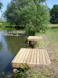 two wooden benches sitting on the side of a river next to a lush green field