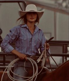 a woman riding on the back of a brown horse wearing a cowboy hat and holding a lasso