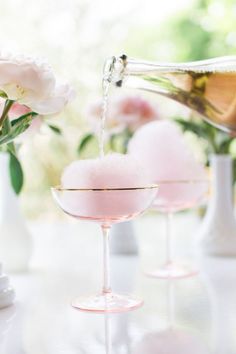 two wine glasses filled with pink liquid and water being poured into the glass for serving