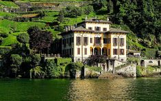 a large house sitting on top of a lush green hillside next to a body of water