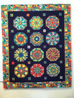 a colorful quilt hanging on the wall next to a white wall with a black background