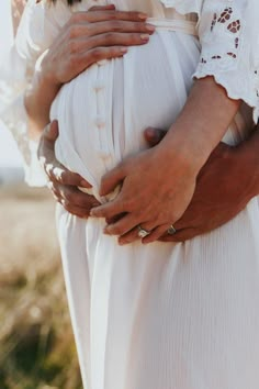 a pregnant woman in a white dress holding her belly